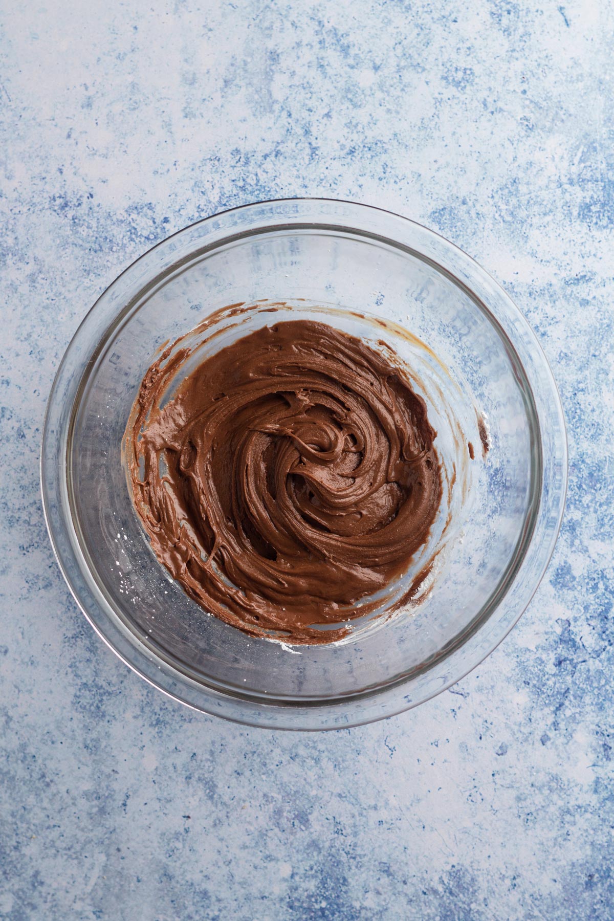 Chocolate filling in a glass bowl on a blue surface.