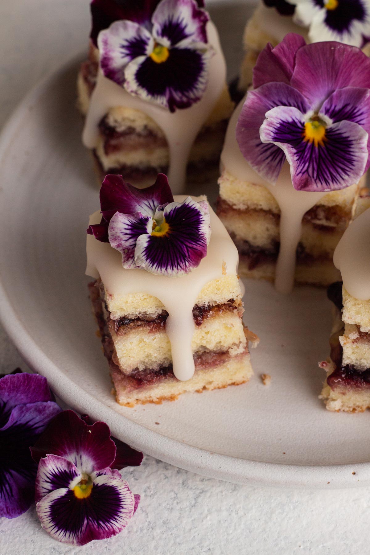 Angled view of plate of glazed petit fours topped with pansy flowers.