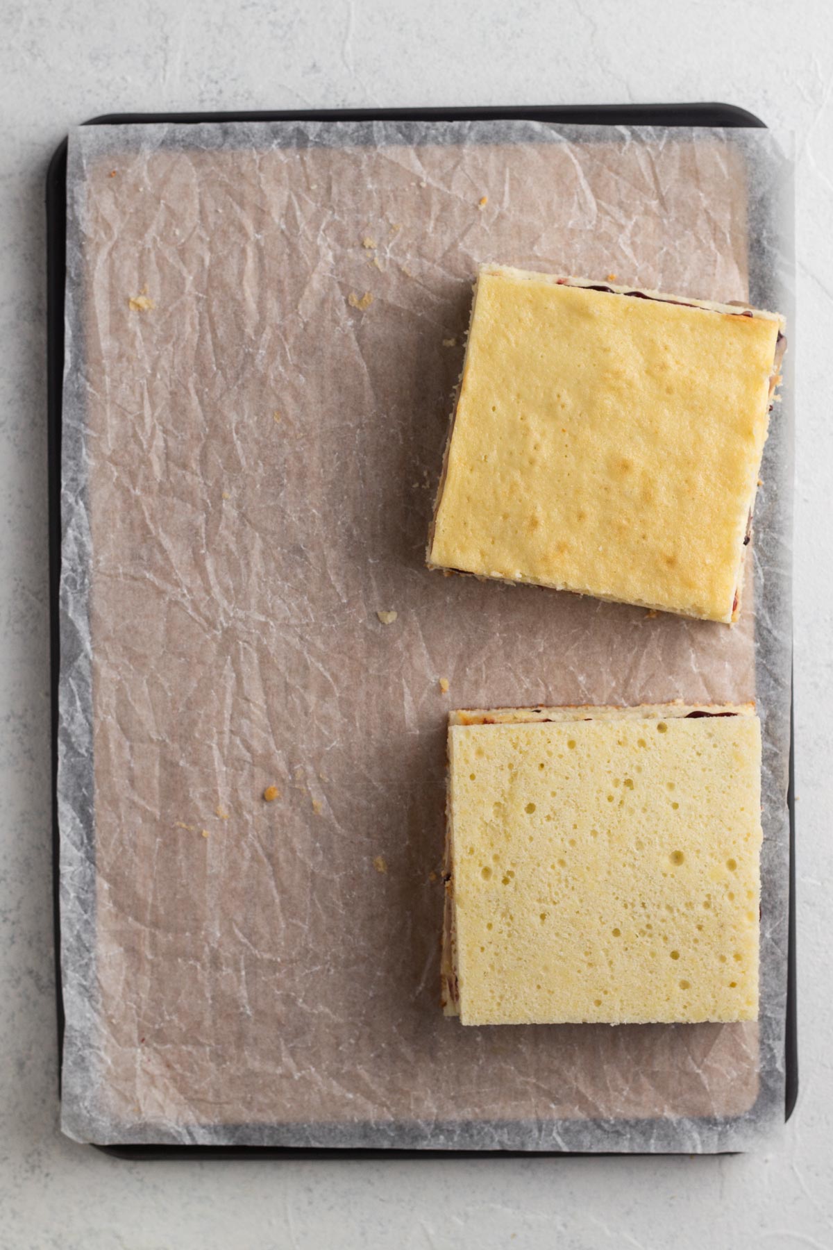 Stacked squares of cake on a wooden cutting board topped with parchment paper.