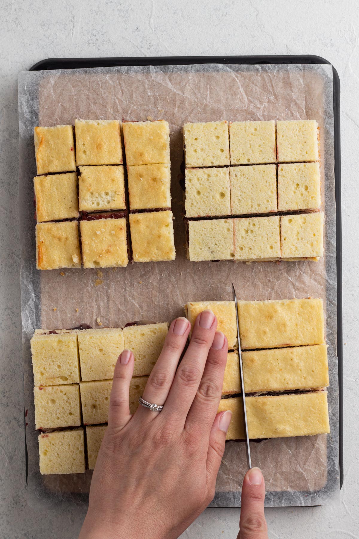 Hands cutting stacked cake squares into smaller tea cakes.