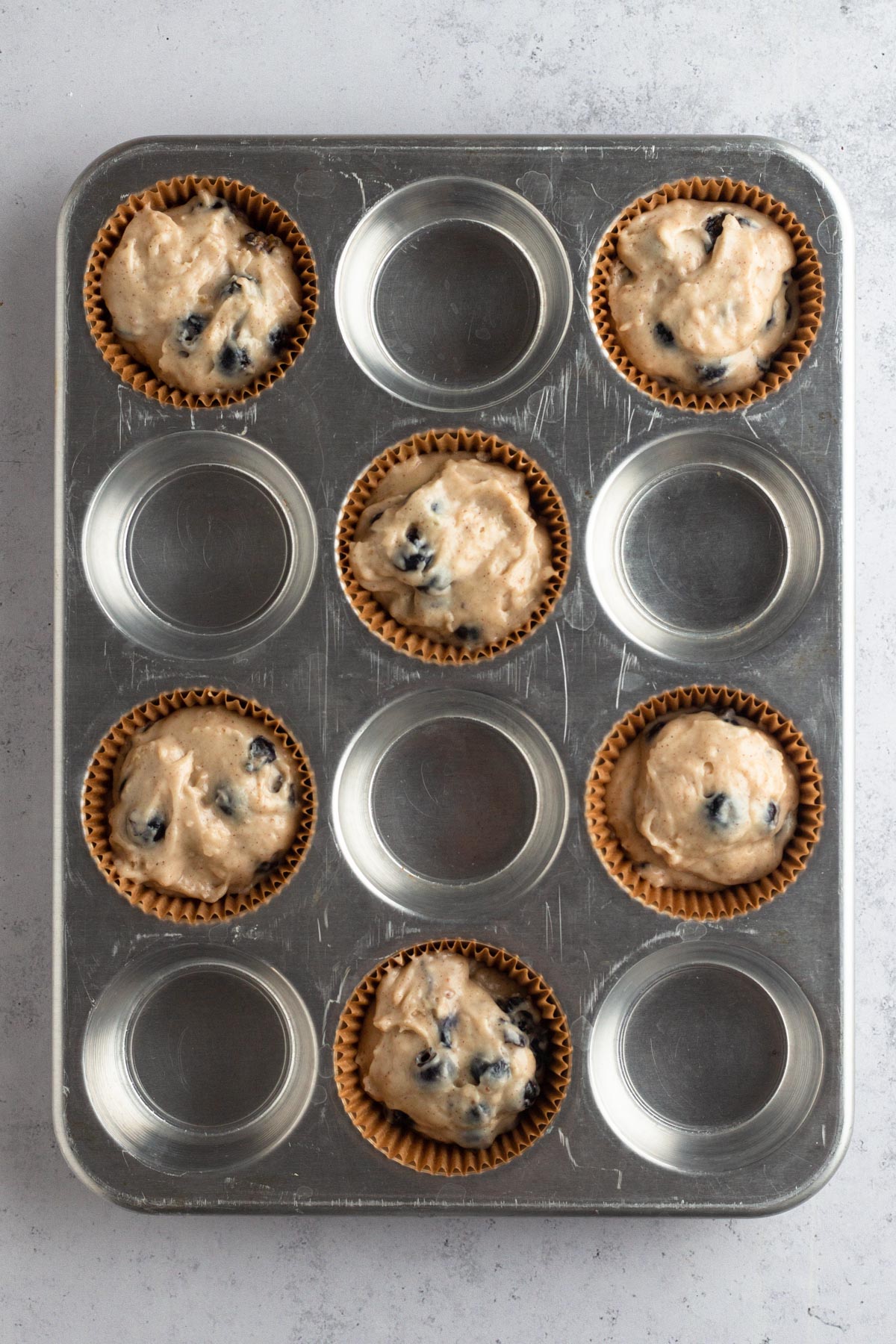 Muffin batter in brown paper liners in a metal muffin pan.