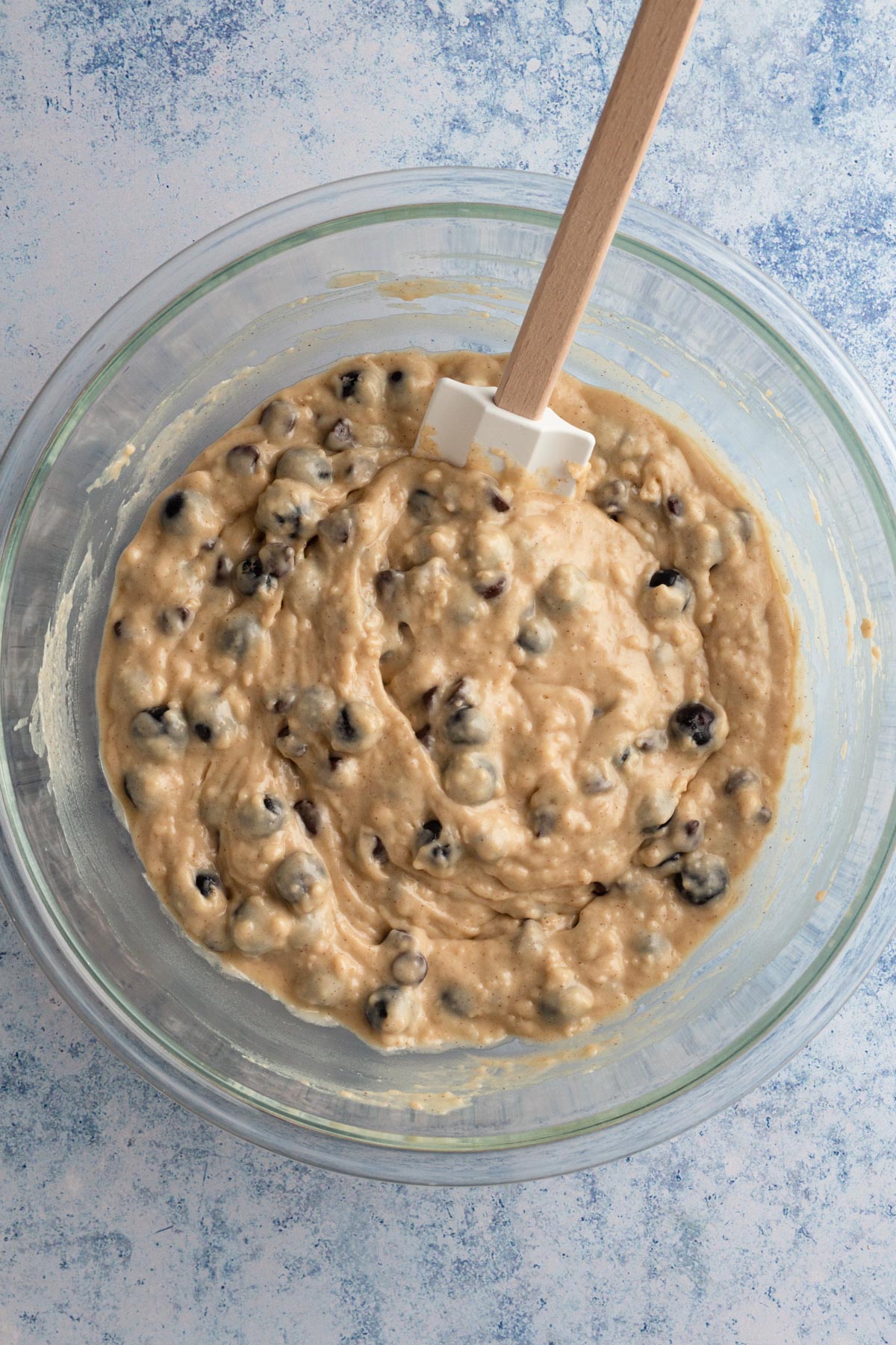 Overhead view of blueberries and chocolate chips blended into muffin batter in a glass bowl.