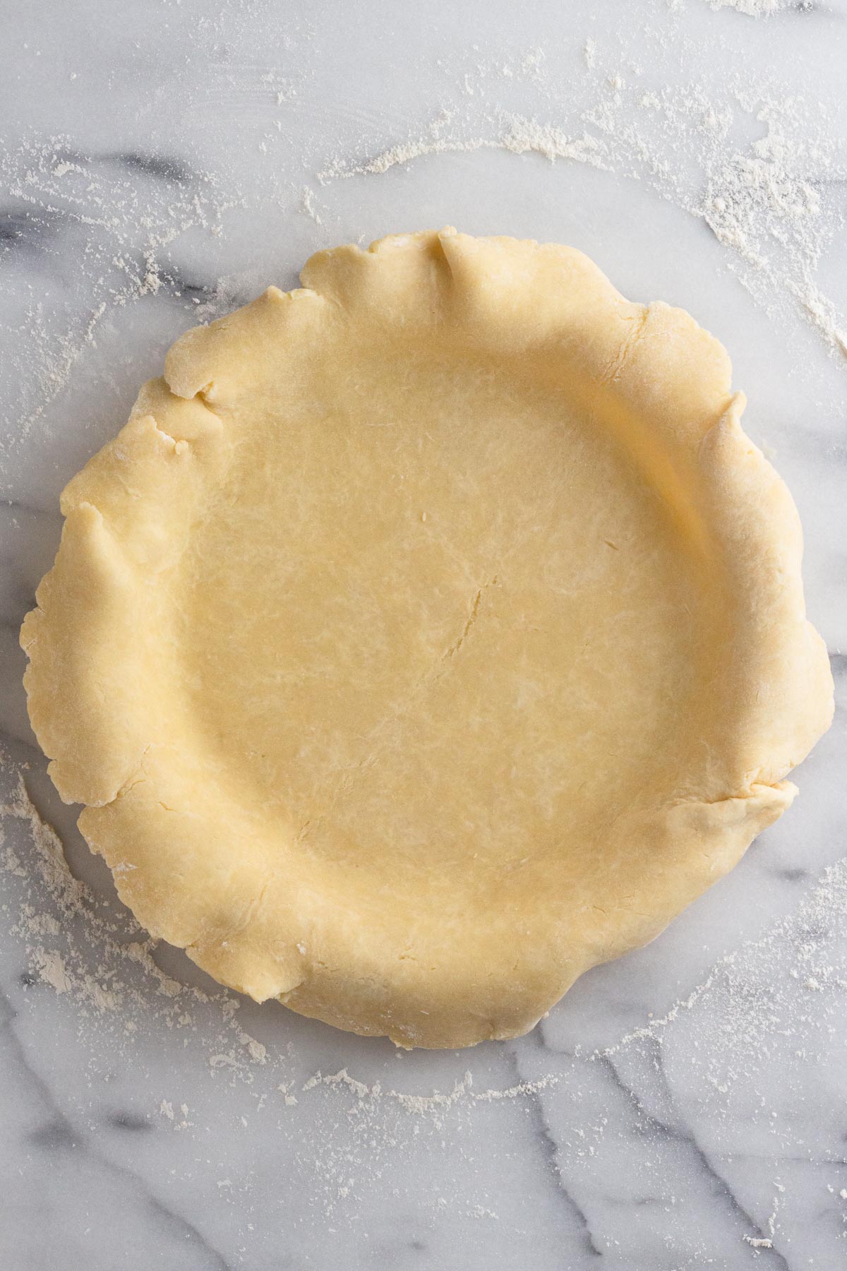 Pie crust in a pie plate on a marble surface.