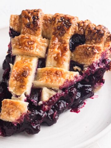 A slice of blueberry pie with a lattice crust on a white plate.