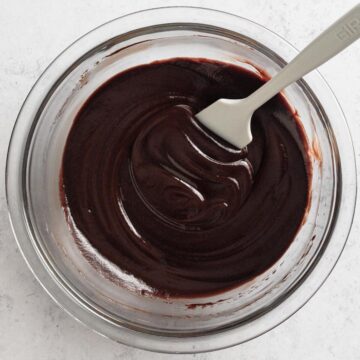 Overhead view of chocolate ganache in a glass mixing bowl with a white rubber spatula.