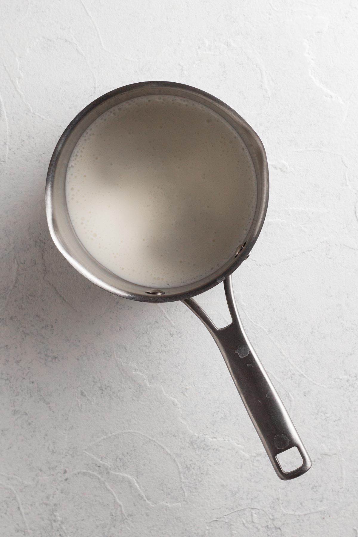 Simmering cream in a metal saucepan on a white surface.