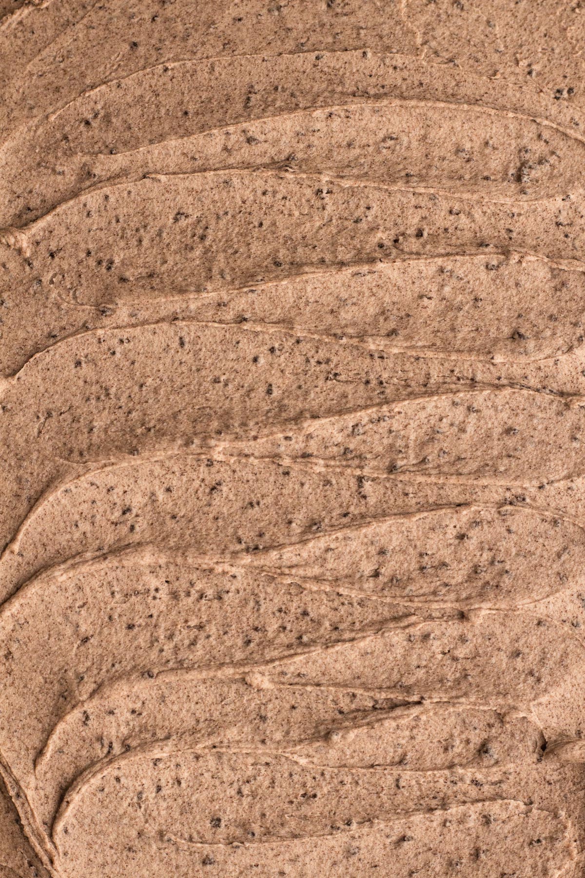 Close-up overhead view of frosting with flecks of crushed cookies spread over a cake.