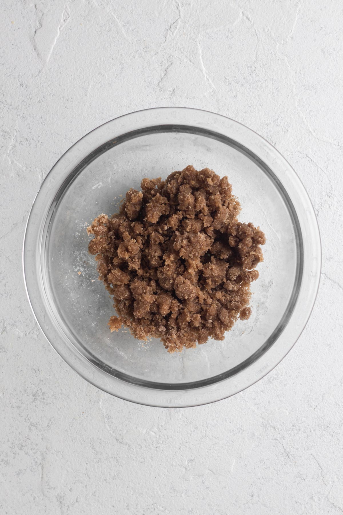 Streusel topping in a glass bowl on a white surface.