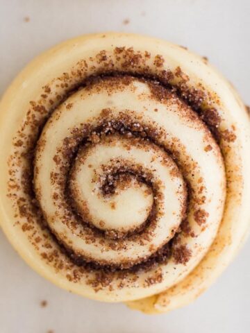 Close-up overhead view of an unbaked cinnamon roll on a white surface.