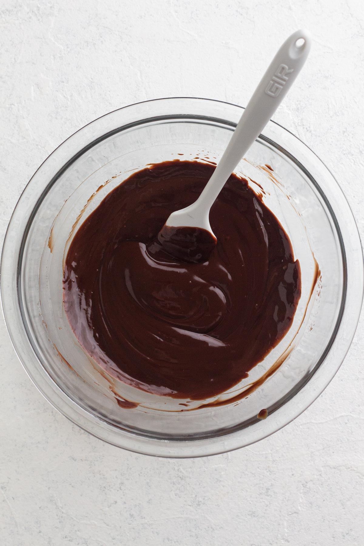 Chocolate ganache in a glass bowl with a white spatula.