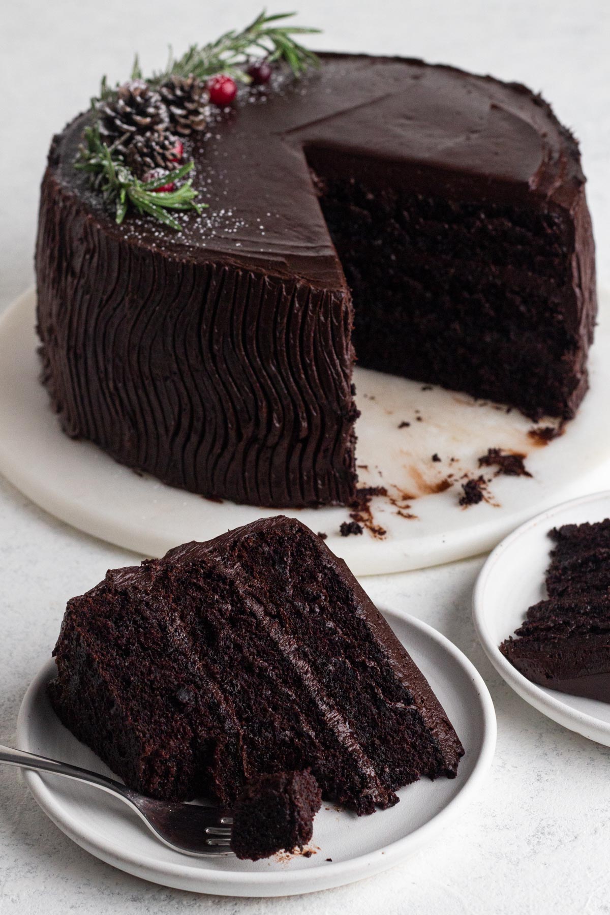 Chocolate-frosted chocolate cake on a marble board with slices of the cake on white plates.
