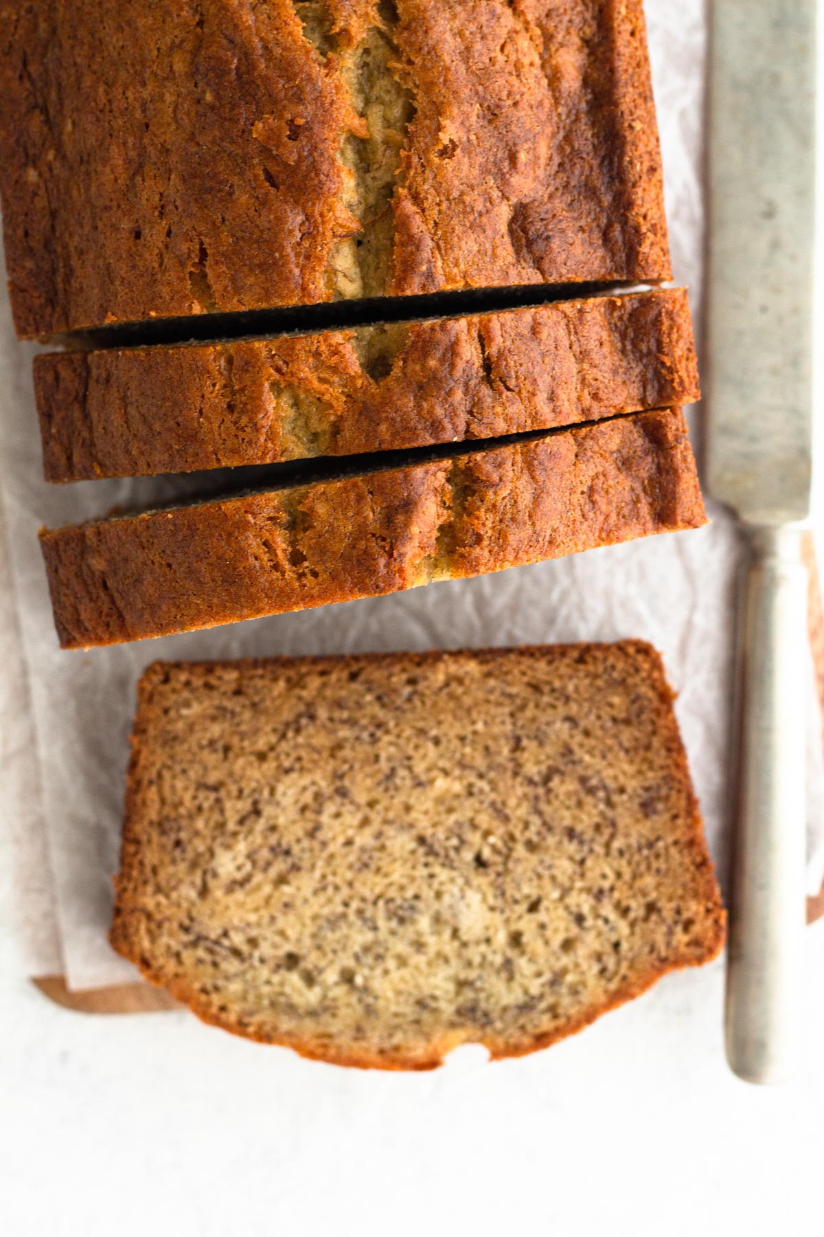 Overhead view of sliced banana bread atop parchment paper with a butter knife.