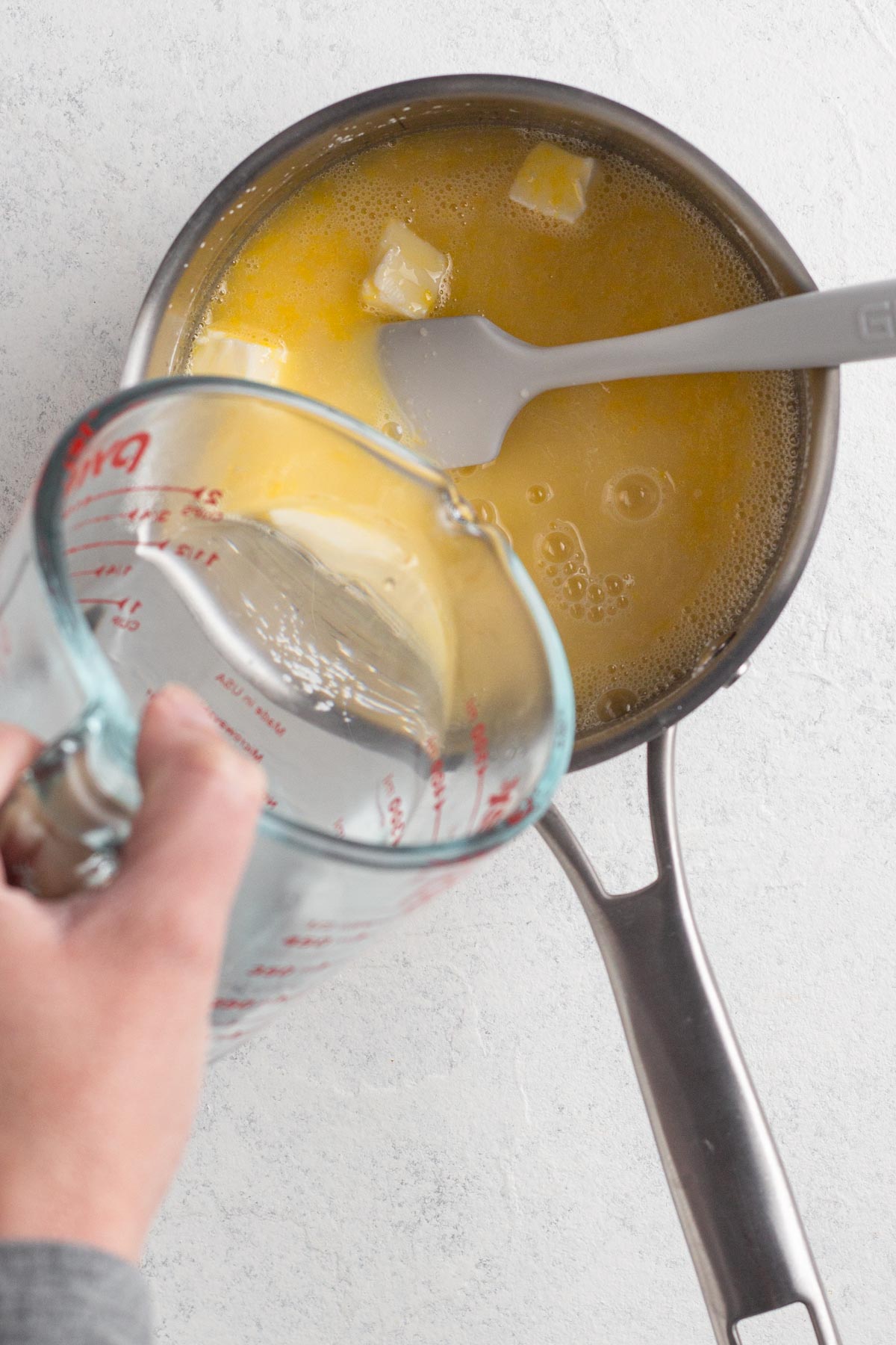 Hand pouring boiling water into a saucepan with sugar, lemon juice, and butter.