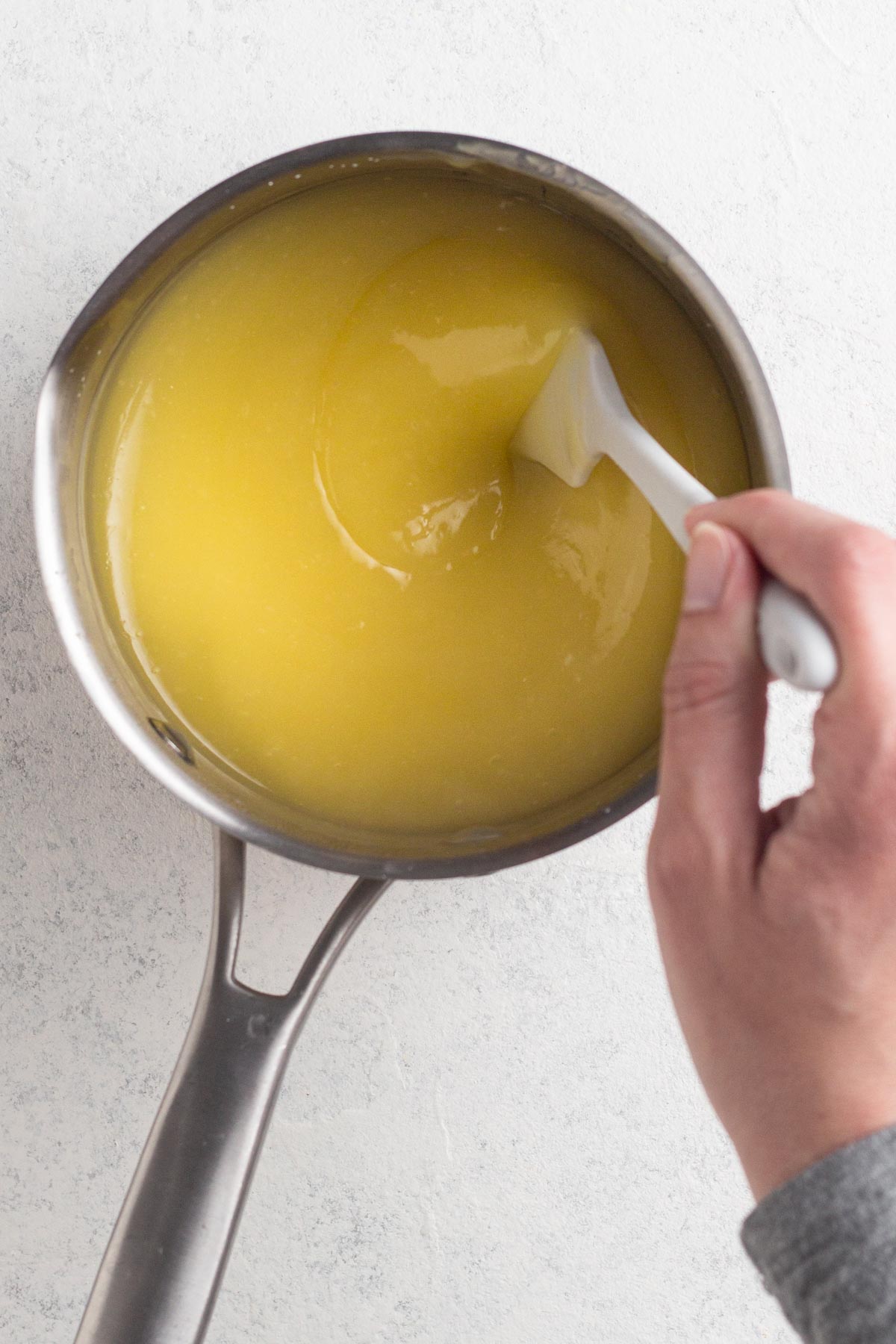Hand stirring thickened lemon curd in a saucepan.