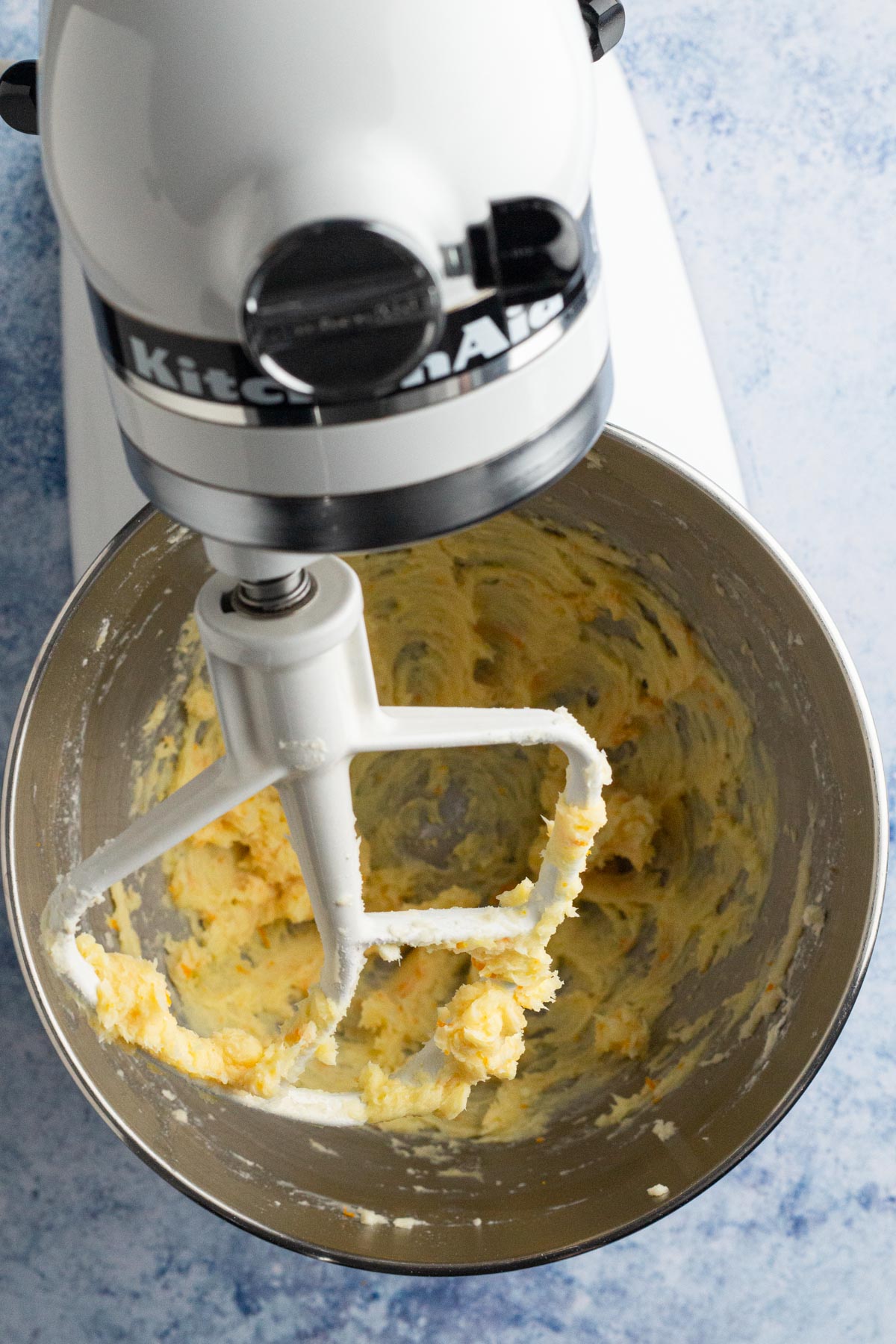 Butter and sugar mixture in a white stand mixer on a blue surface.