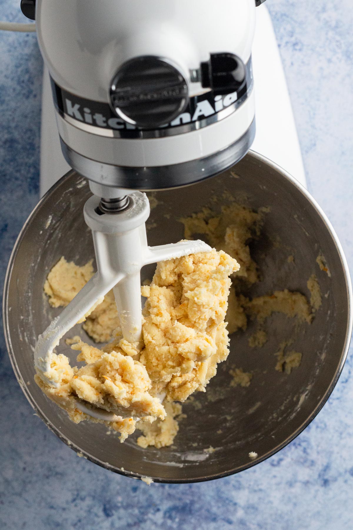 Cookie dough in the bowl of a white Kitchen Aid stand mixer on a blue background.