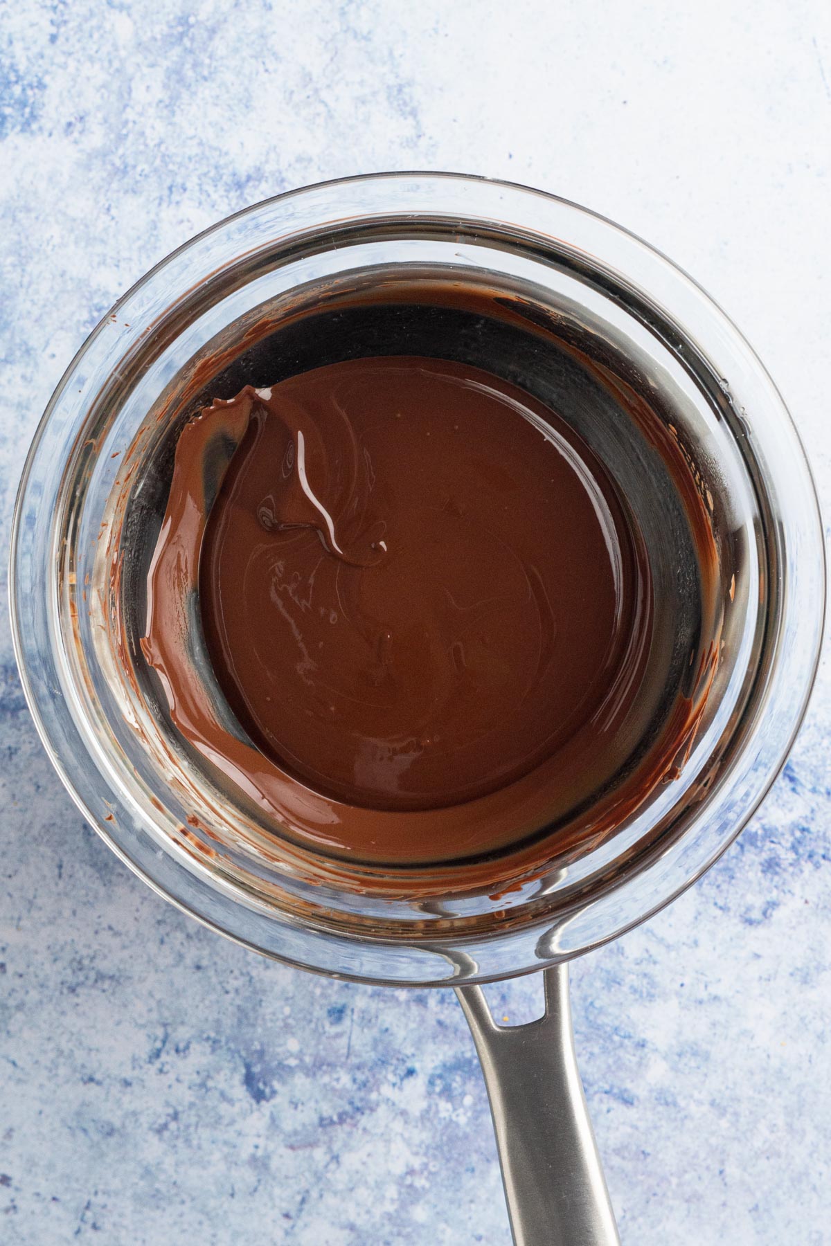 Melted chocolate in a DIY double boiler on a blue surface.