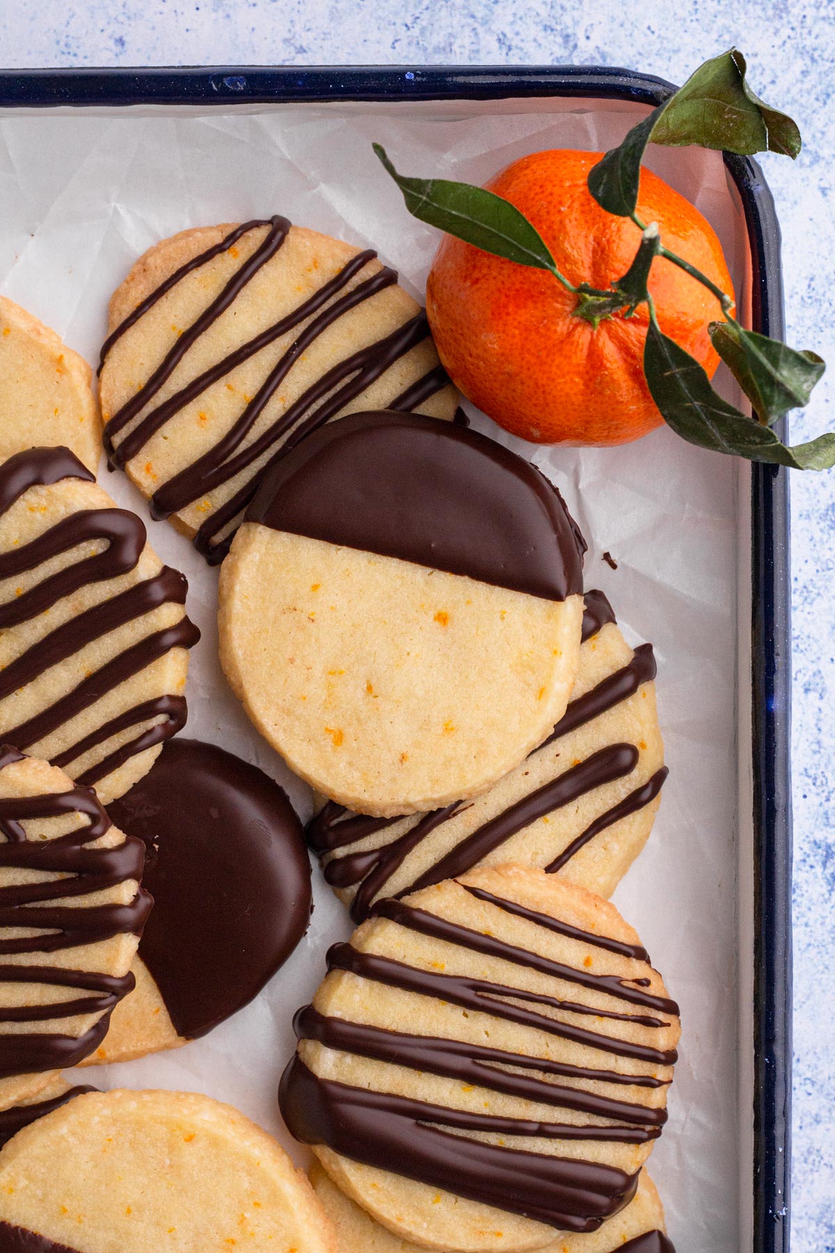 Overhead view of chocolate-dipped shortbread cookies stacked on a tray with an orange.