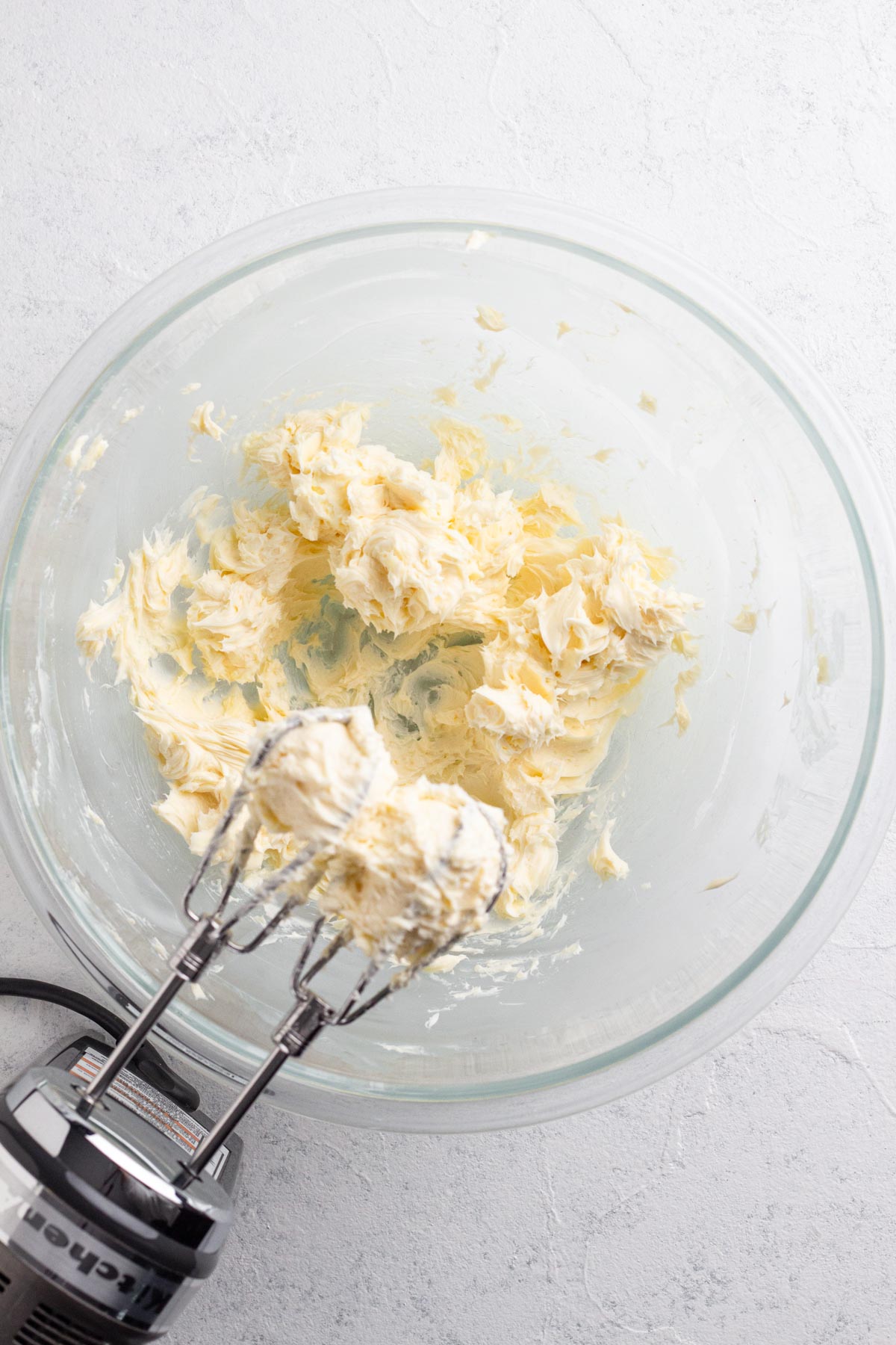 Beaten butter in a glass mixing bowl with a hand mixer.