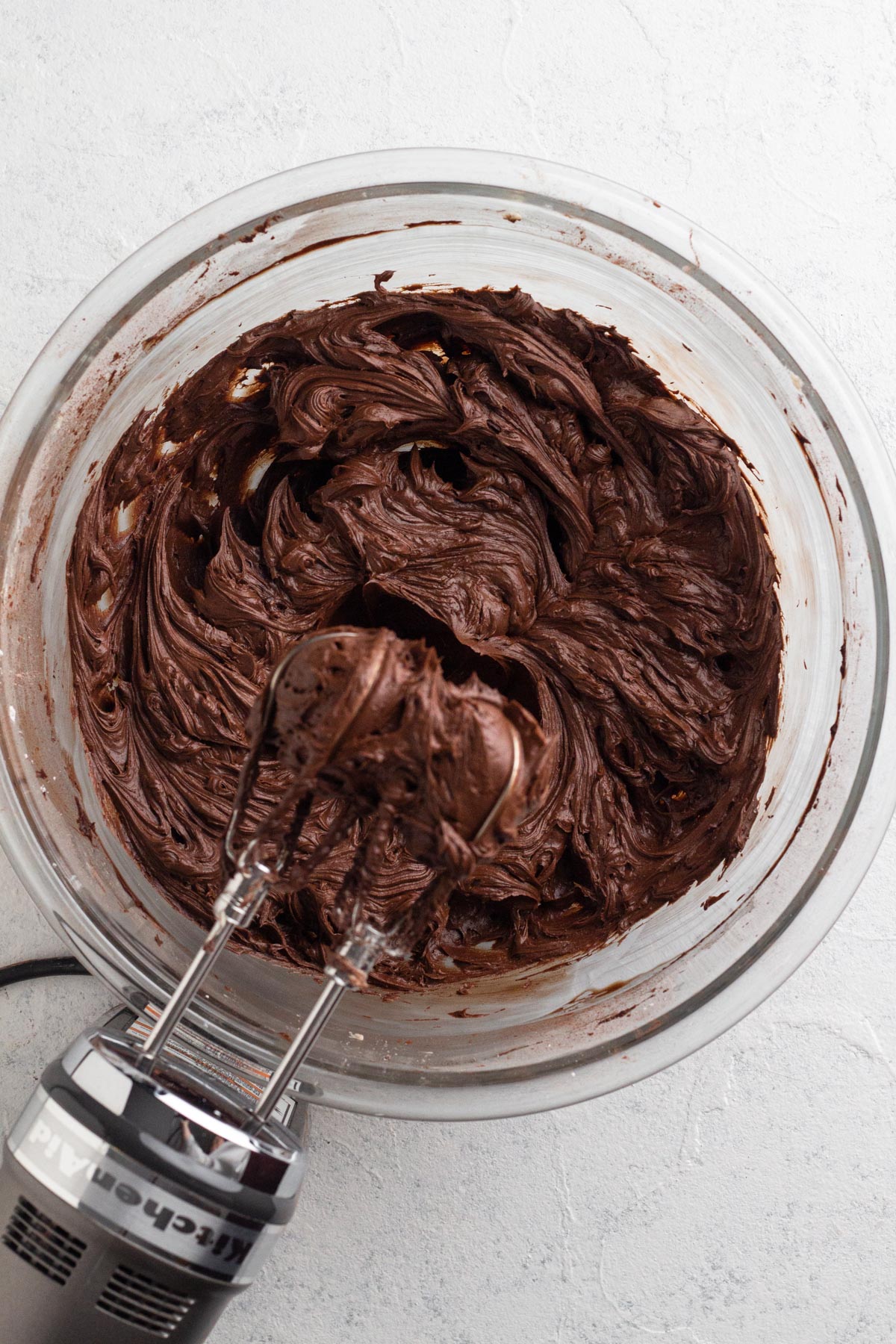 Creamy frosting after ganache is added in a glass mixing bowl with a hand mixer.