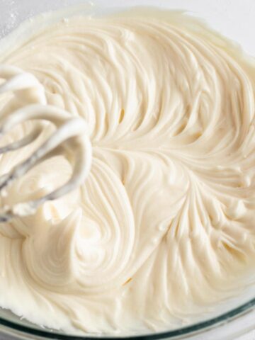 Close up view of cream cheese frosting in a glass mixing bowl with electric beaters.