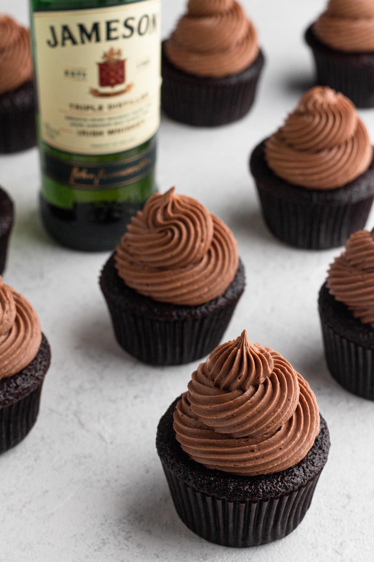 Chocolate cupcakes topped with swirls of chocolate frosting surrounding a bottle of Jameson Irish whiskey.