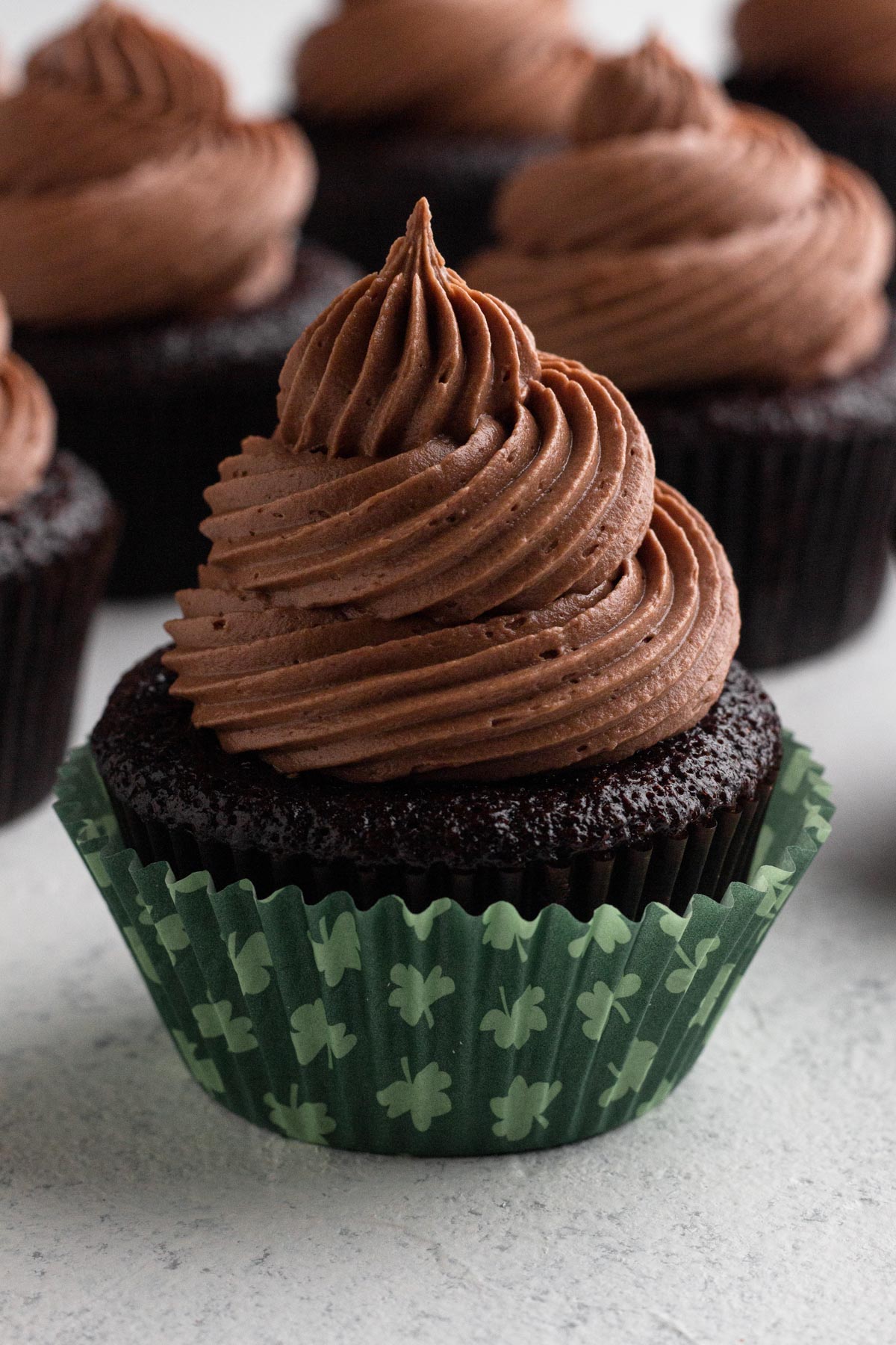 Chocolate frosting swirled on top of a chocolate cupcake in a green cupcake paper with shamrocks.
