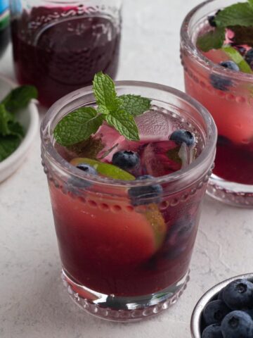 Close up of mocktail in a glass with fresh blueberries, a sprig of mint, and a slice of lime.