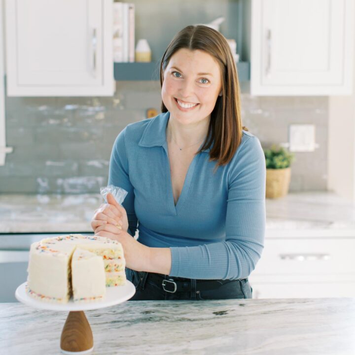 Allison leaning over the kitchen counter piping frosting onto a cake.