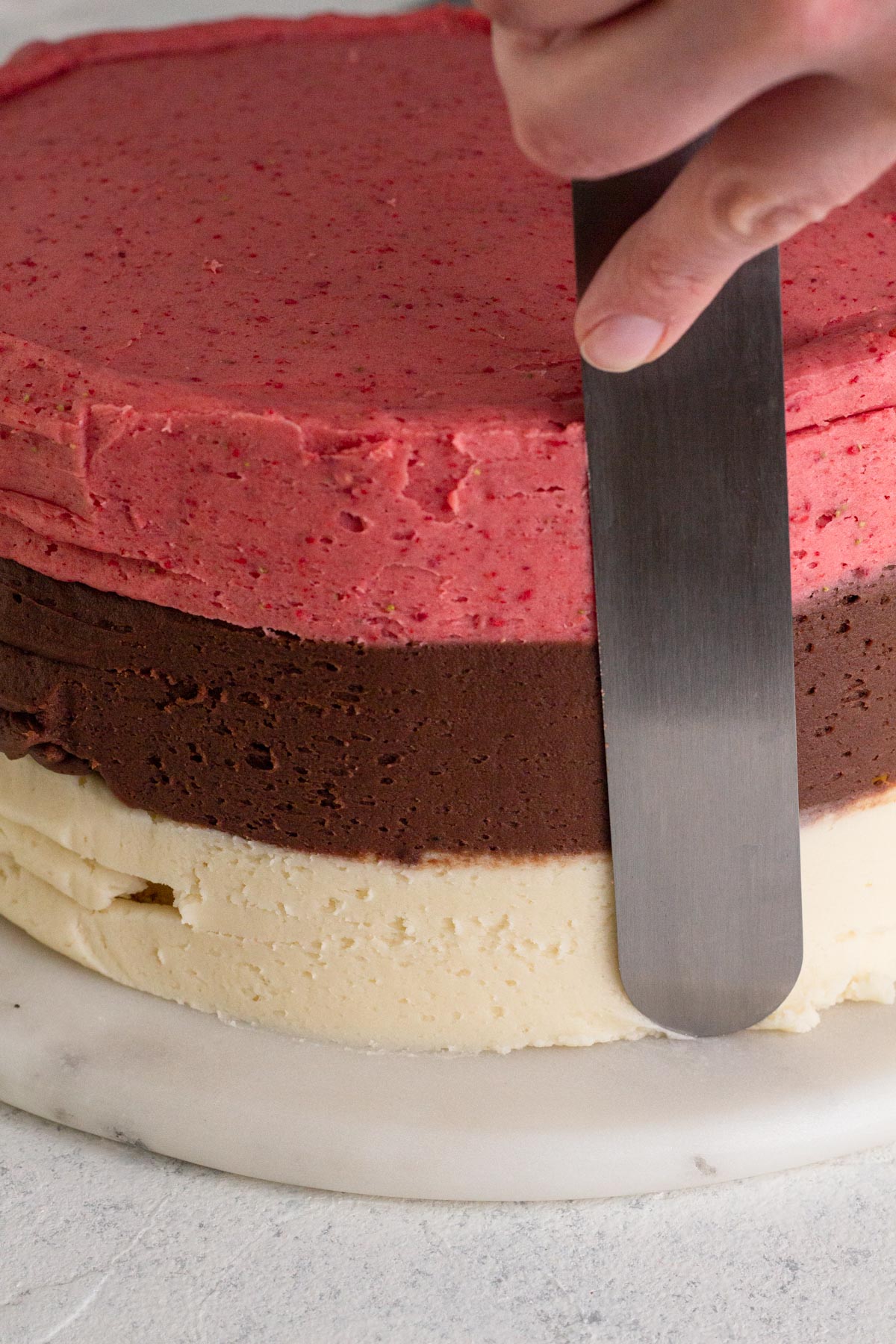 Hand smoothing sides of frosted cake with a large offset spatula.