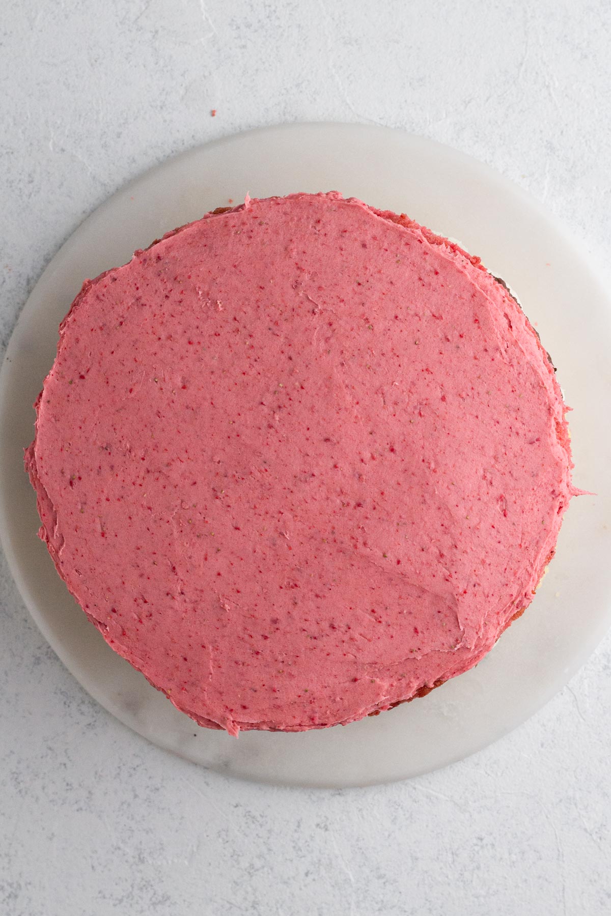 Stacked layer cake topped with strawberry frosting.