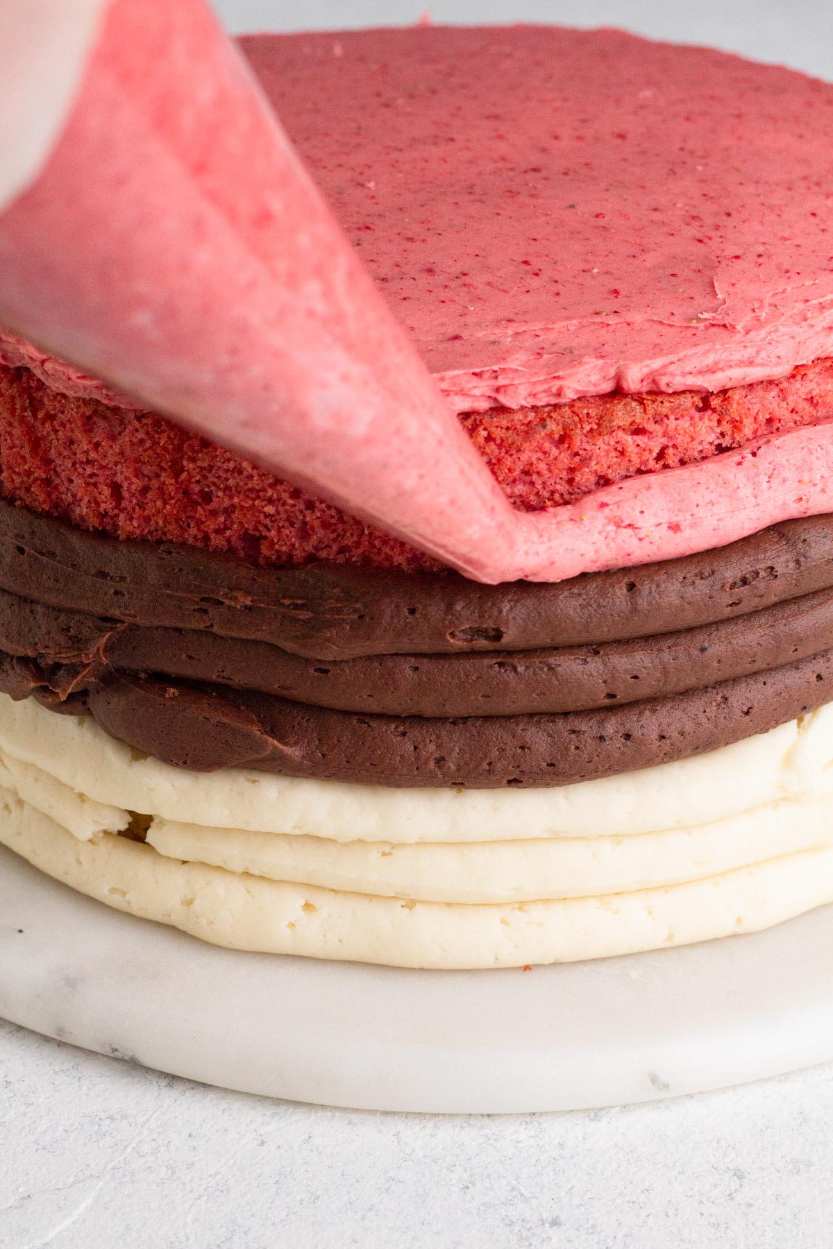 Piping strawberry frosting around the sides of a layer cake.