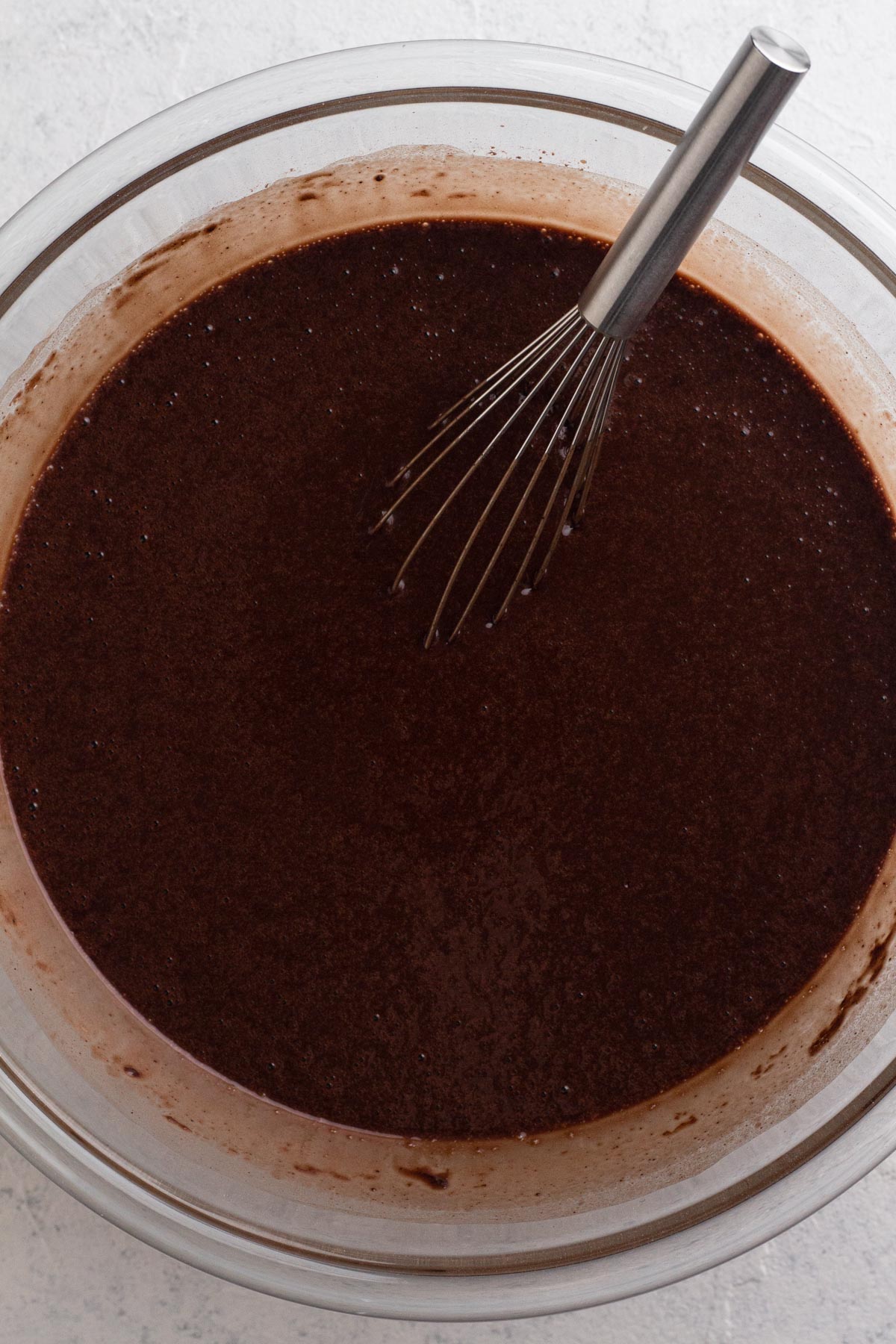 Chocolate cake batter with hot coffee in a glass mixing bowl.
