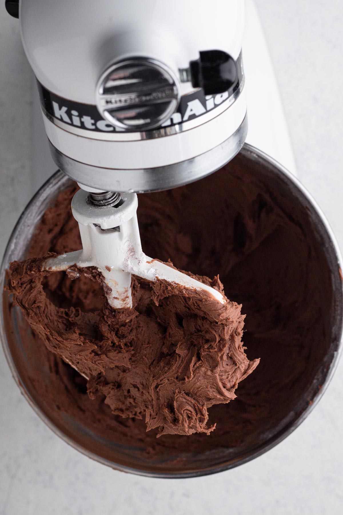 Chocolate frosting in the bowl of a stand mixer.