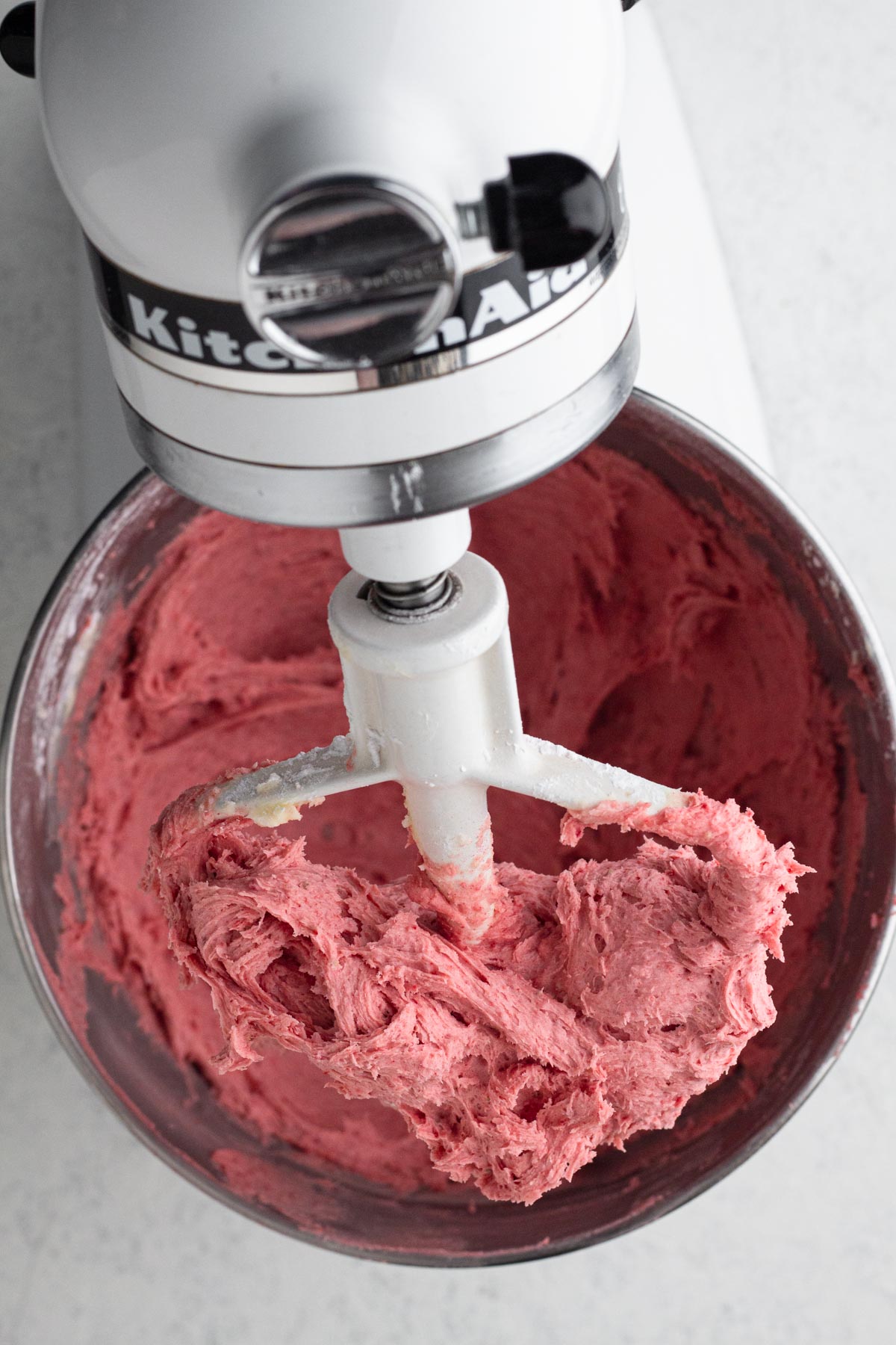 Strawberry frosting in the bowl of a stand mixer.