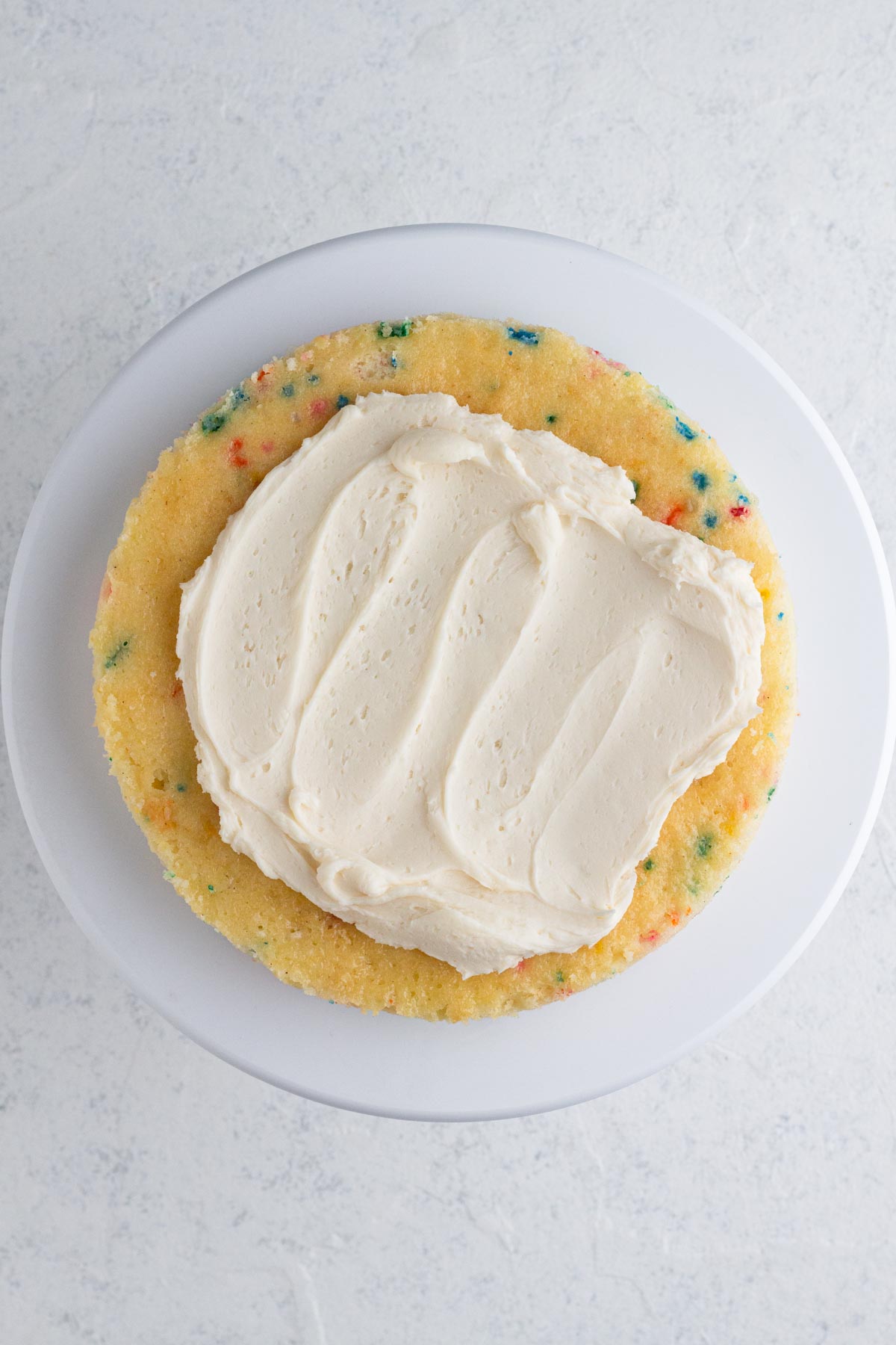 Vanilla frosting being spread onto a sprinkle-filled cake.