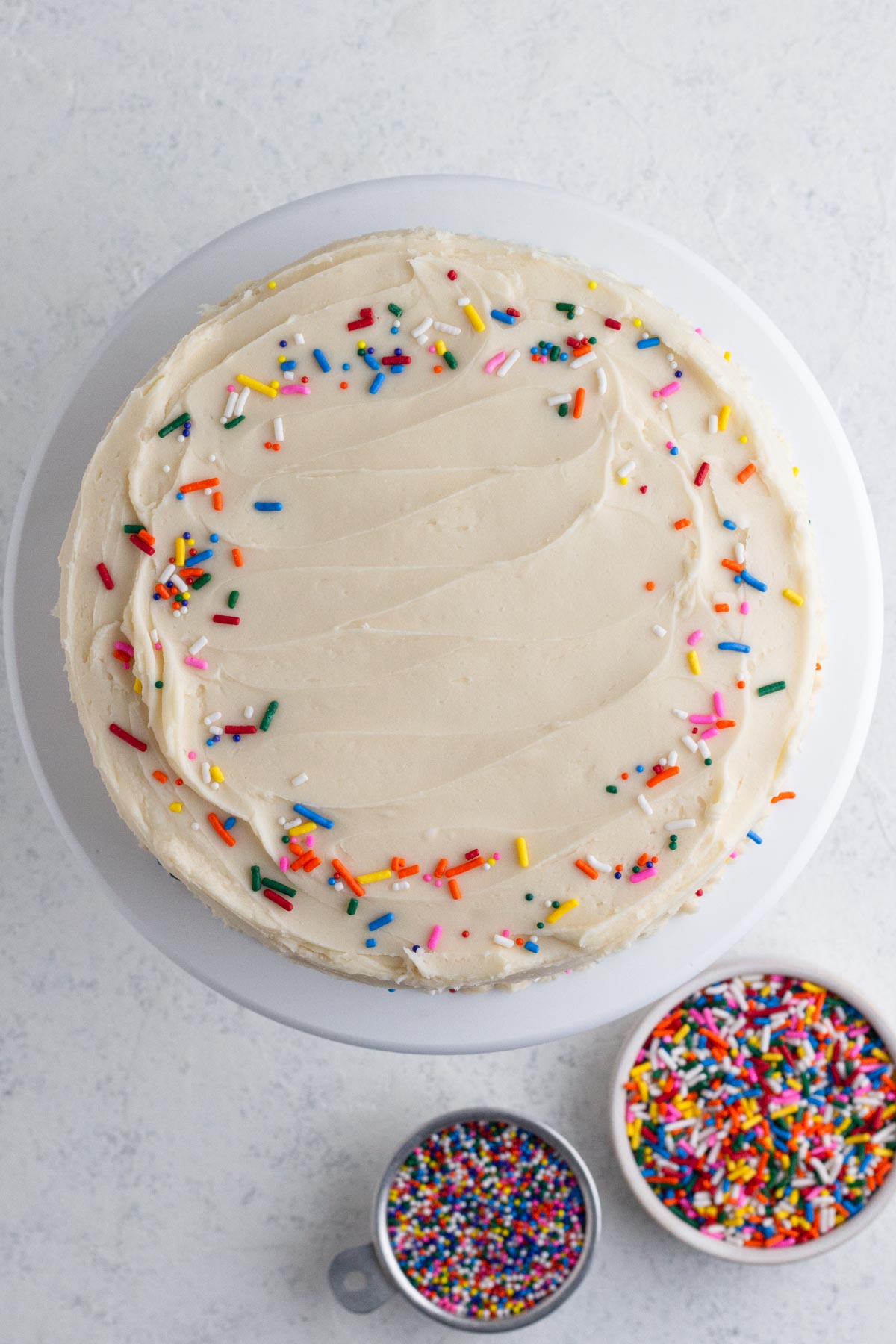 Overhead view of a cake decorated with vanilla frosting and rainbow sprinkles.