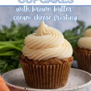 A carrot cake cupcake topped with a swirl of cream cheese frosting on a speckled plate surrounded by carrots with a text overlay.