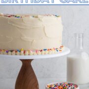 Cake decorated with vanilla frosting and sprinkles on a wooden cake stand with a text overlay.