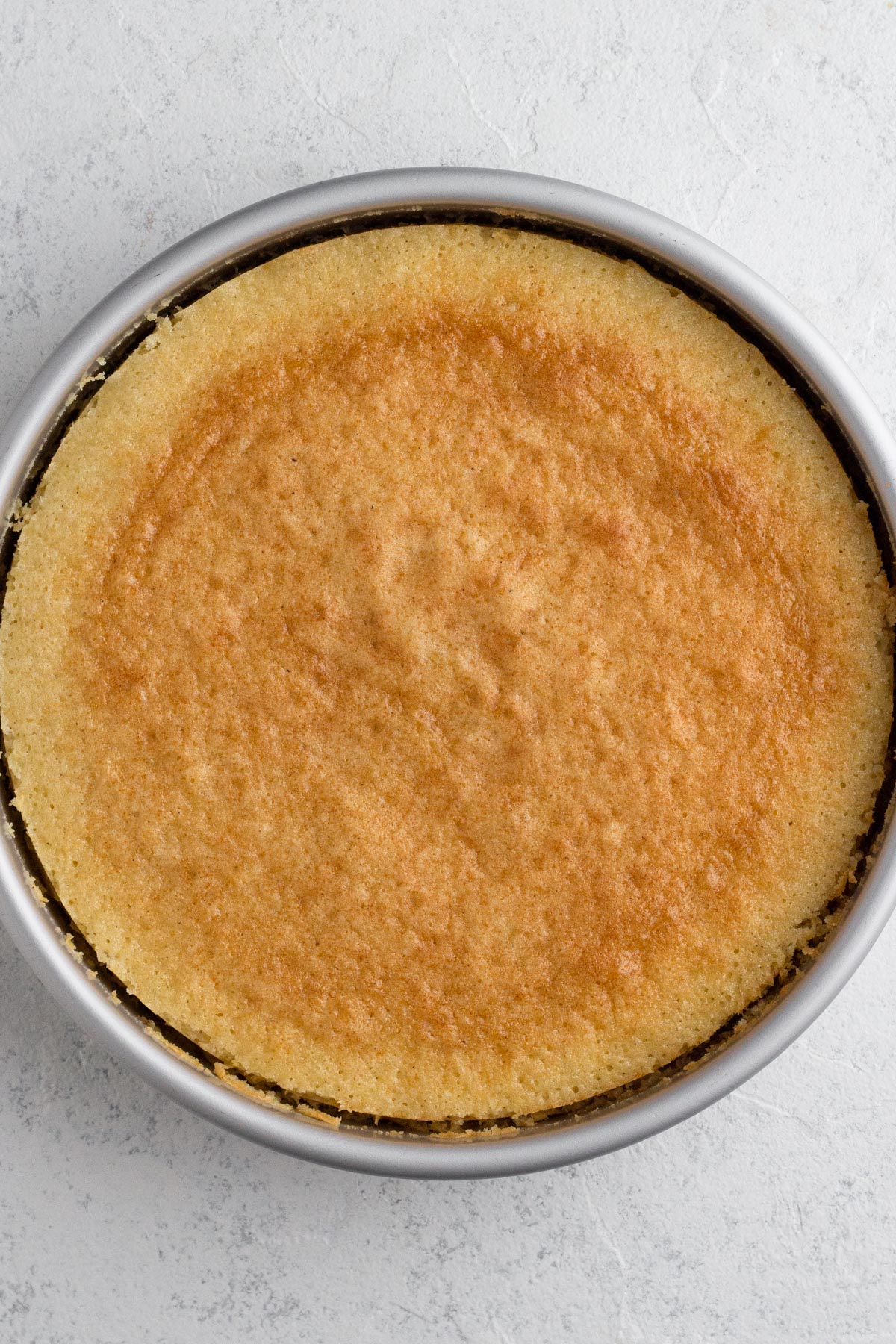 Baked vanilla cake in a round metal pan.