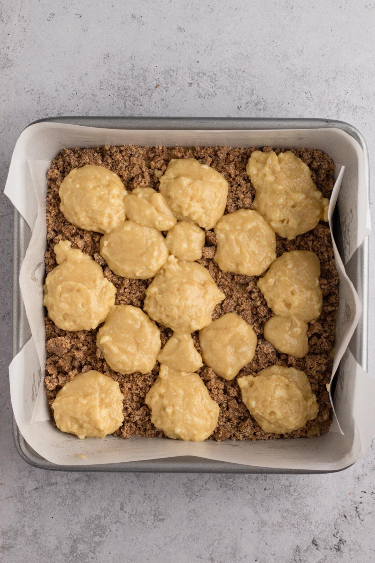 Dollops of batter over crumb filling in a square baking pan.