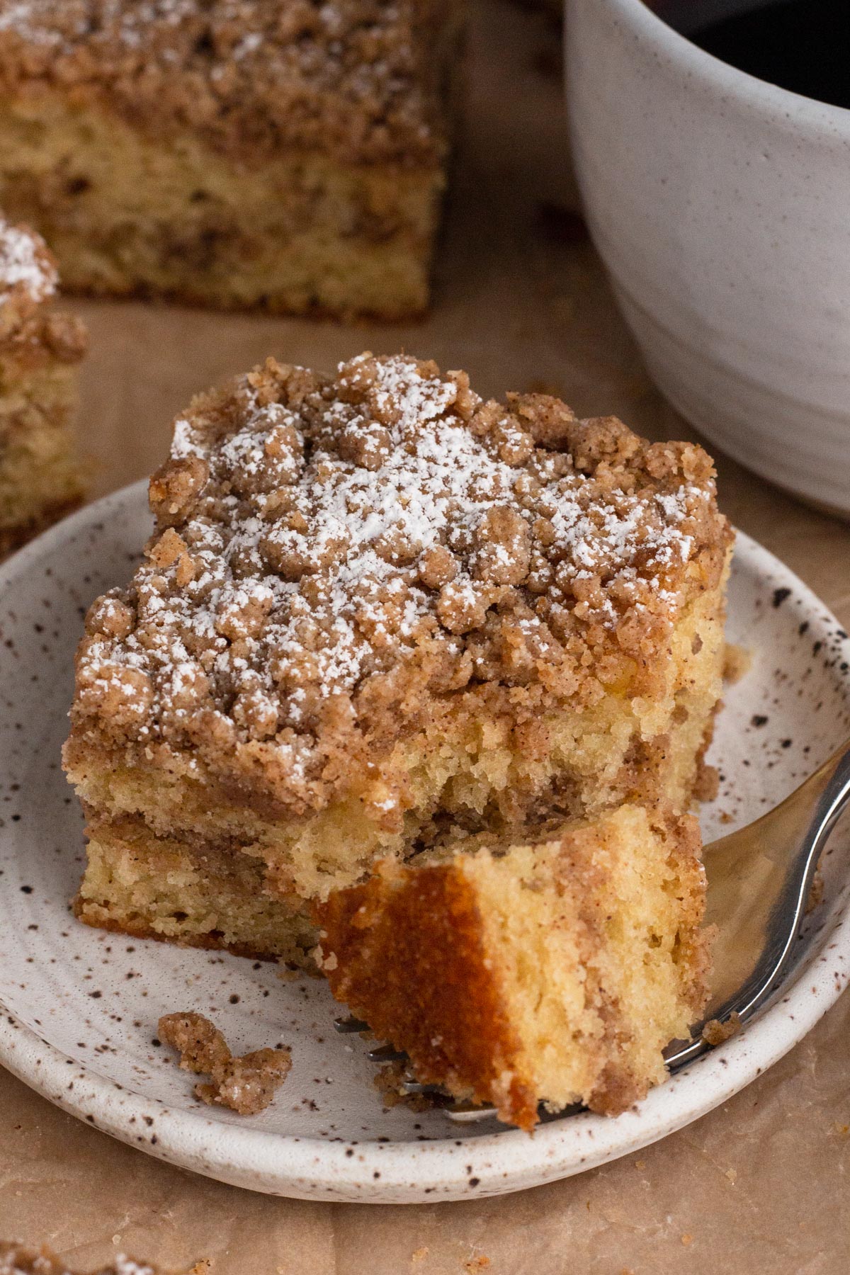 A slice and forkful of coffee cake on a speckled plate with a mug of coffee.