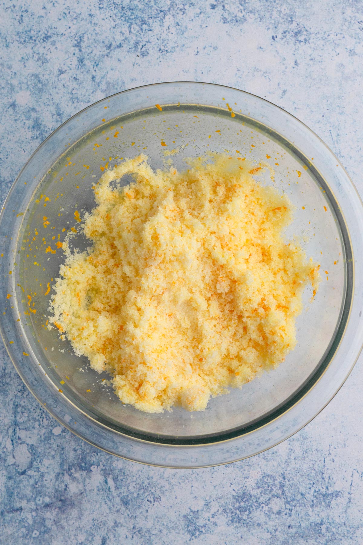 Orange zest rubbed into sugar in a glass mixing bowl.