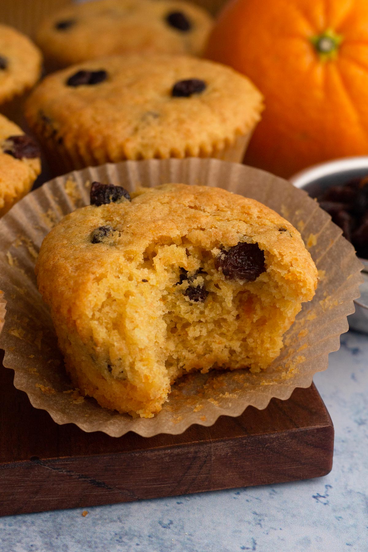 A bitten muffin on a wooden cutting board with a whole orange.