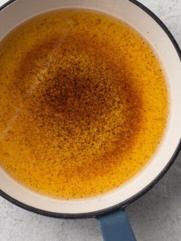 Close up view of brown butter in a blue-handled skillet.
