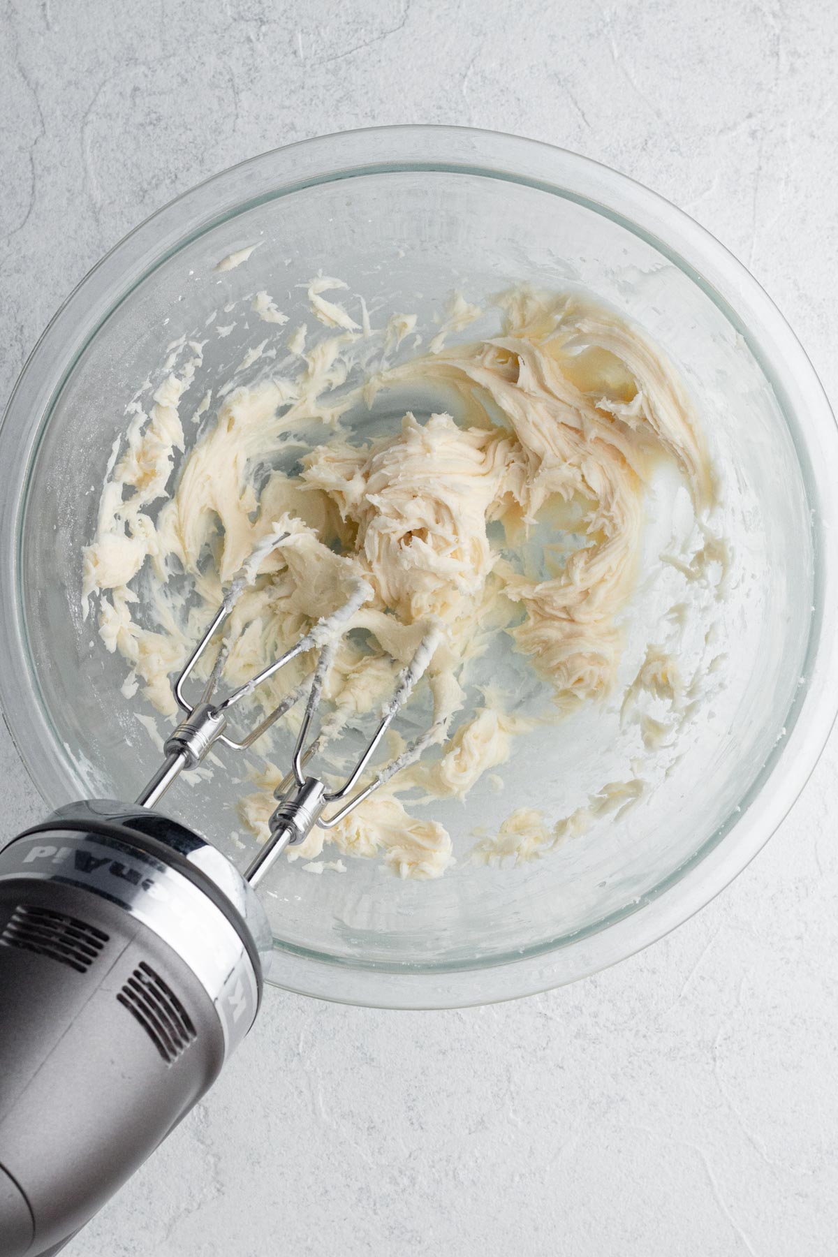 Buttercream frosting in a glass mixing bowl with an electric hand mixer.