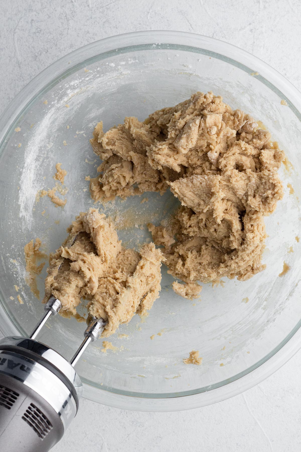 Cookie dough in a glass mixing bowl with an electric hand mixer.