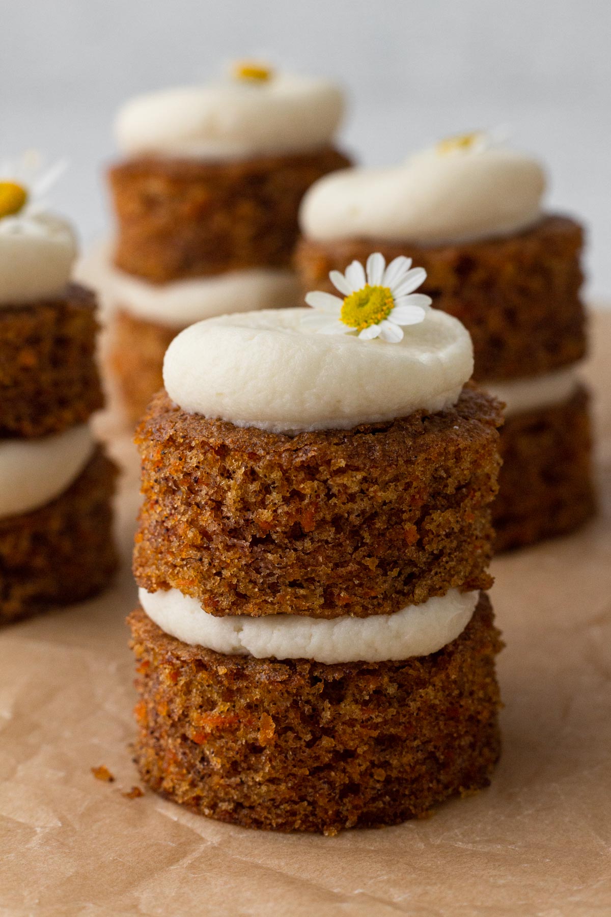 Bite-sized carrot cakes stacked with cream cheese frosting and topped with fresh chamomile flowers.