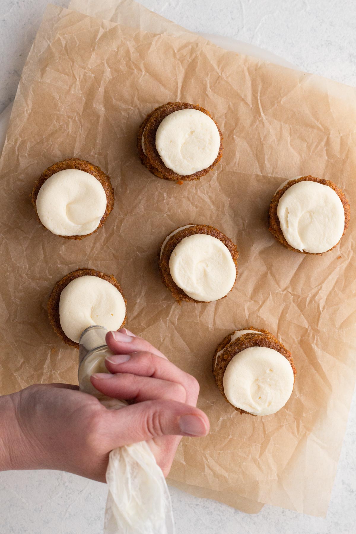 Hand piping frosting onto tiny round cakes.