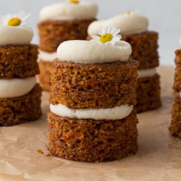 Small carrot cakes stacked with cream cheese frosting and topped with fresh chamomile flowers.
